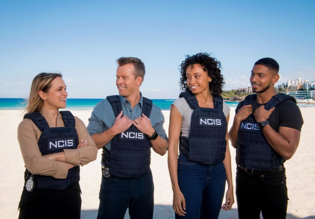 L-R: Tuuli Narkle as AFP Liaison Officer Constable Evie Cooper, Todd Lasance as AFP Liaison Officer Sergeant Jim  'JD' Dempsey, Olivia Swann as NCIS Special Agent Captain Michelle Mackey and Sean Sagar as Special Agent DeShawn Jackson at Bondi Beach, on the set of NCIS: Sydney. - PHOTO CREDIT: Daniel Asher Smith/Paramount+